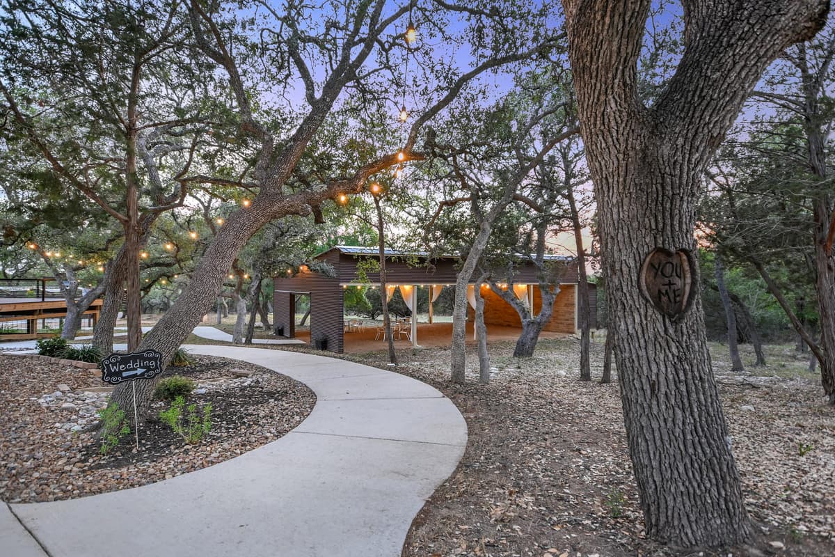 A smooth concrete pathway winds through oak trees toward Prima Vista's covered pavilion