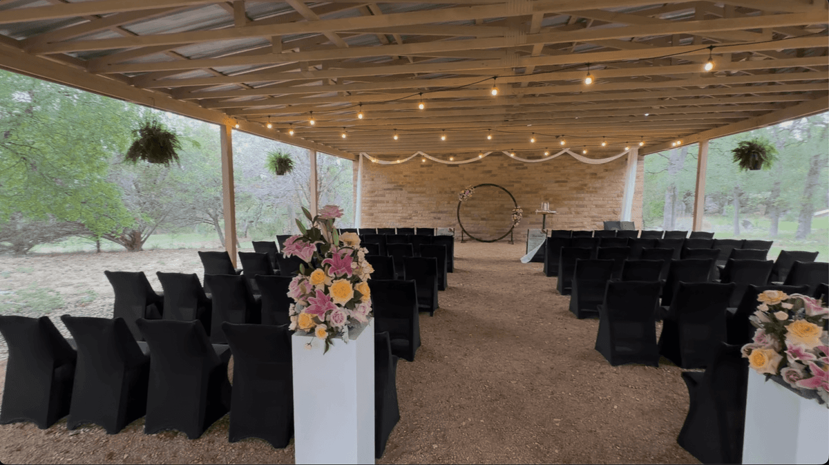 Covered ceremony pavilion at Prima Vista with string lights, florals, and black chairs set for a wedding
